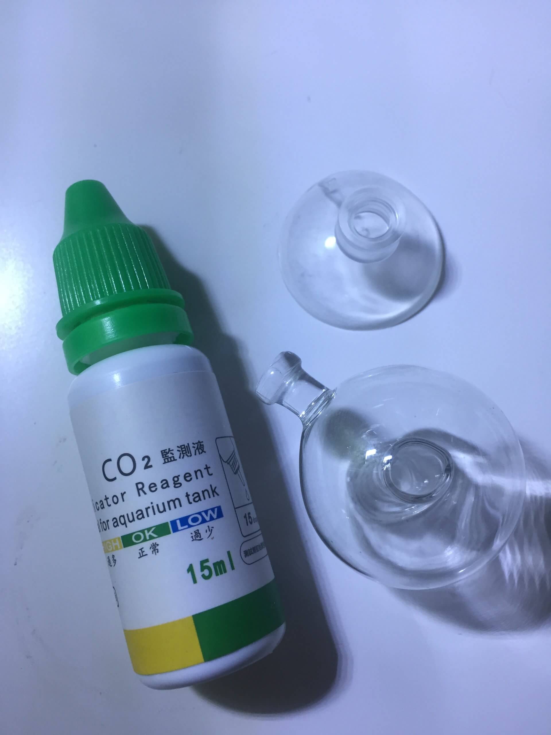 Eine kleine CO₂-Testflasche und zwei durchsichtige Glas-Drop-Checker für Aquarien liegen auf einem weißen Hintergrund
