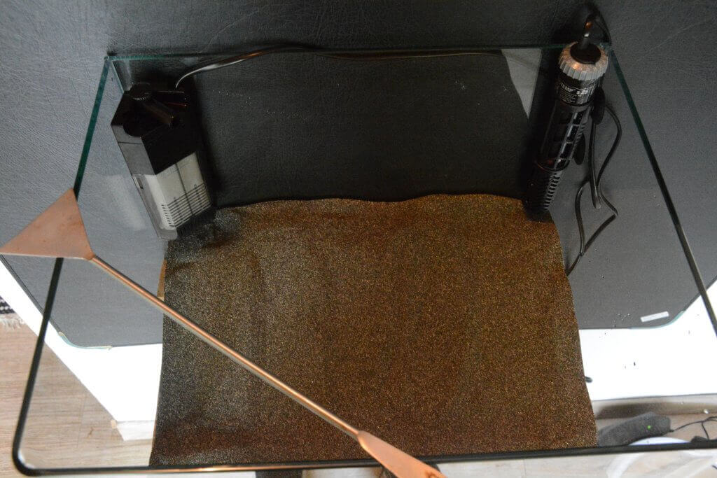 Leeres Glasaquarium mit Sandboden, Innenfilter und Heizgerät rechts und links angebracht, aus der Vogelperspektive